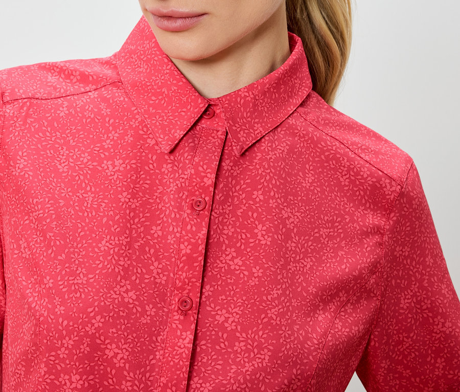 Gros plan d'une femme portant une chemise rouge à motifs floraux et à manches courtes.