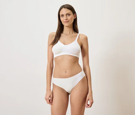 Femme debout en soutien-gorge et culotte blancs sur fond clair.