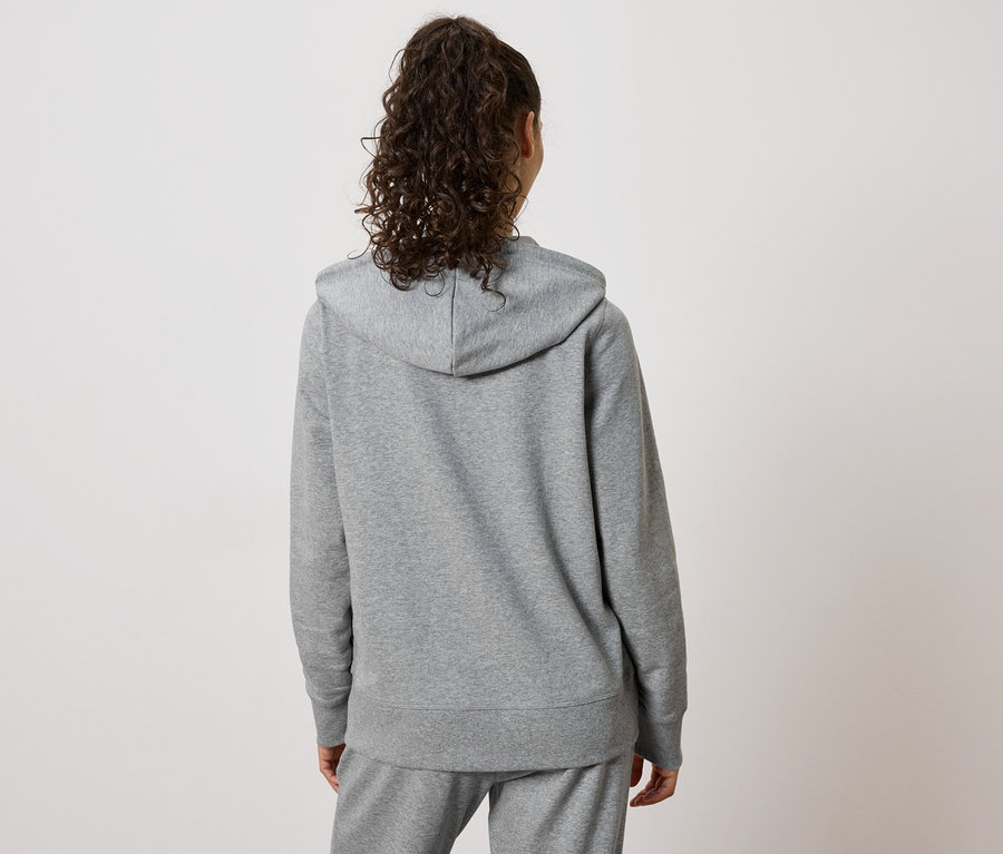 Vue arrière d'une femme aux cheveux bouclés portant un sweat à capuche gris et un pantalon de jogging.