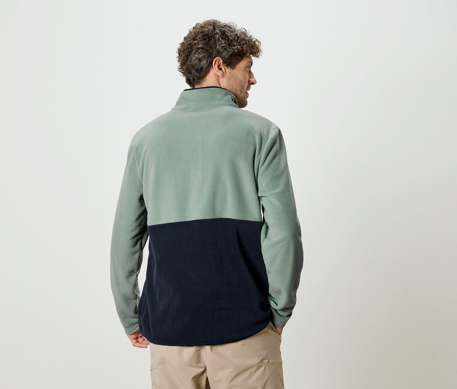 Homme vu de dos portant un pull en polaire bicolore vert et bleu marine et un pantalon beige.