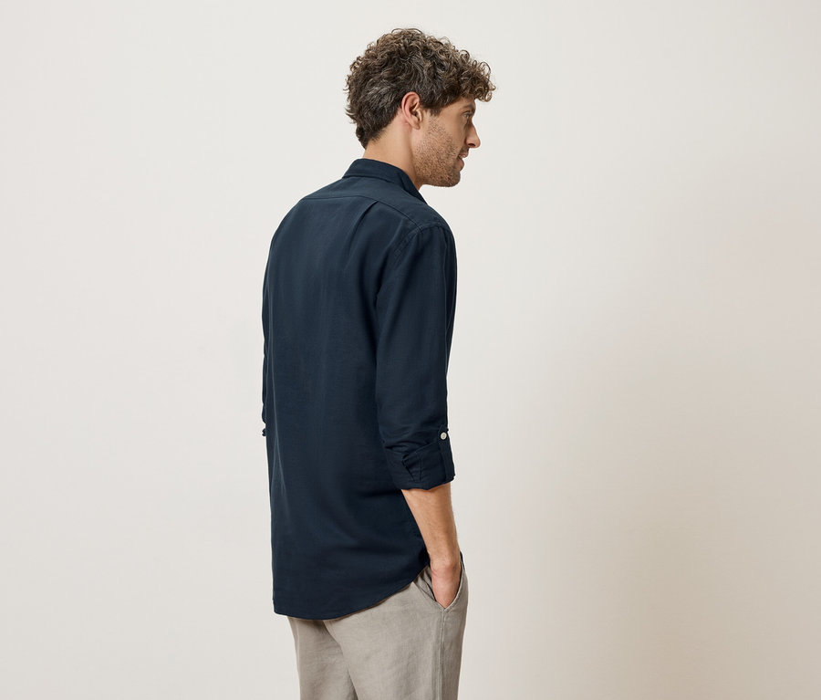 Homme vu de dos portant une chemise bleu marine et un pantalon gris.