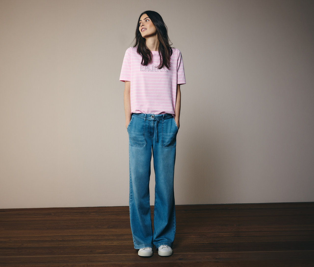 Une femme les mains dans les poches porte un t-shirt CECIL à rayures roses et un jean.