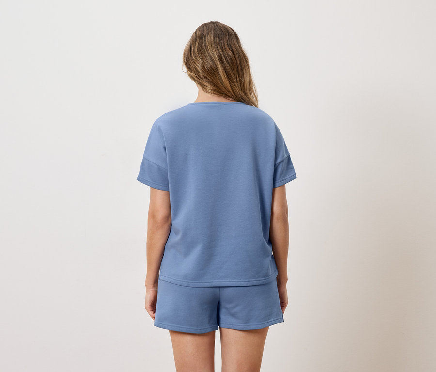 Vue arrière d'une femme aux longs cheveux bruns portant un t-shirt bleu et un short.