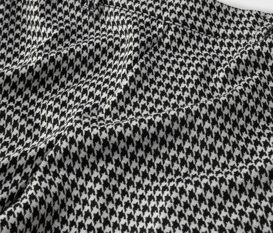 Gros plan d'un vêtement avec un motif pied-de-poule noir et blanc et une couture suggérée.