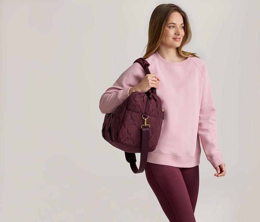 Femme portant un pull rose et un legging bordeaux avec un sac matelassé bordeaux sur l'épaule.