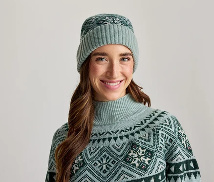 Femme souriante portant un bonnet vert clair et un pull assorti à motifs.