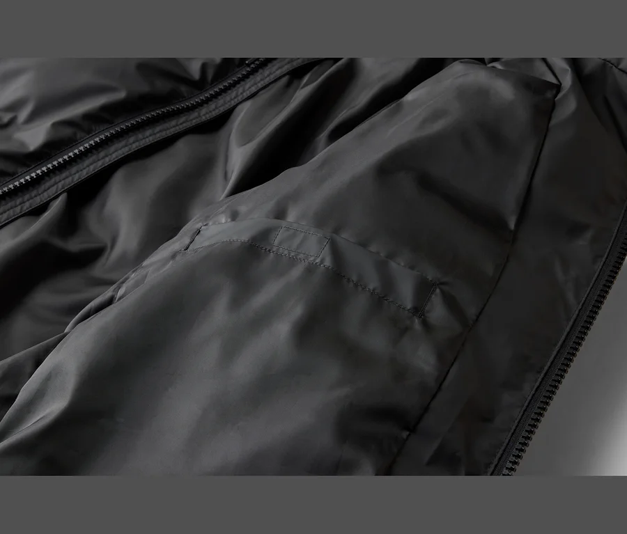 Gros plan d'une veste noire en tissu lisse et légèrement brillant, montrant une fermeture éclair noire et un détail de couture horizontale sur le côté gauche.