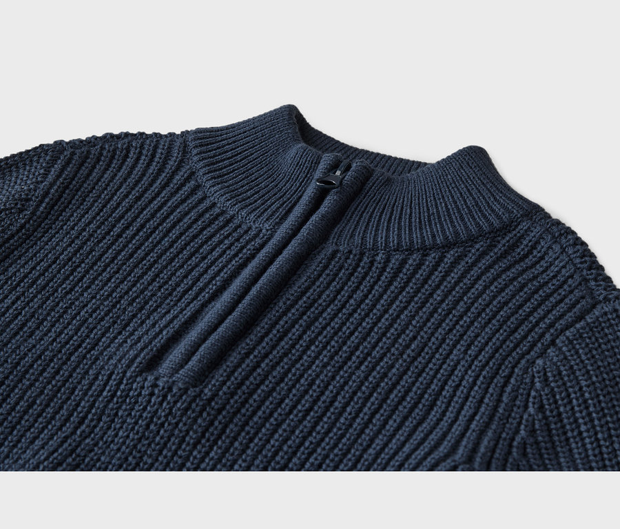 Gros plan d'un pull en maille côtelée bleu marine avec un col montant et une fermeture éclair quart de zip foncée.