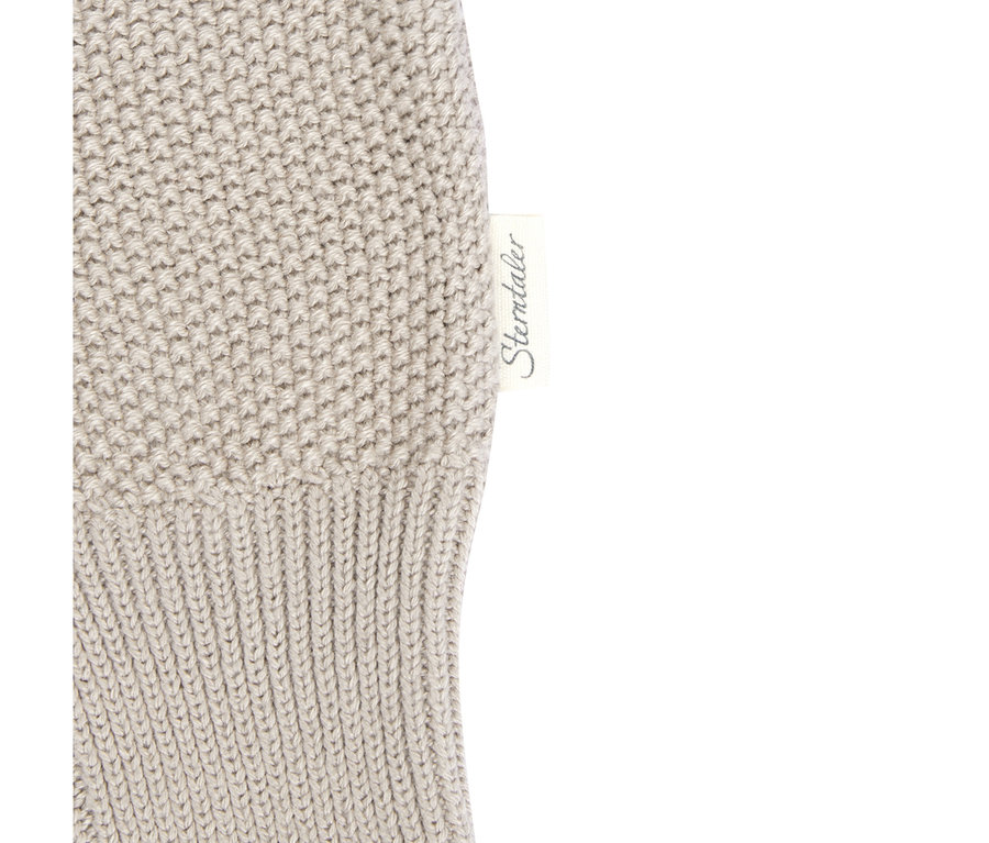 Gros plan sur un pantalon tricoté bébé Sterntaler beige clair, montrant une étiquette de marque blanche avec le texte « Sterntaler » sur une section en tricot côtelé, à côté d'une section en tricot plus dense.