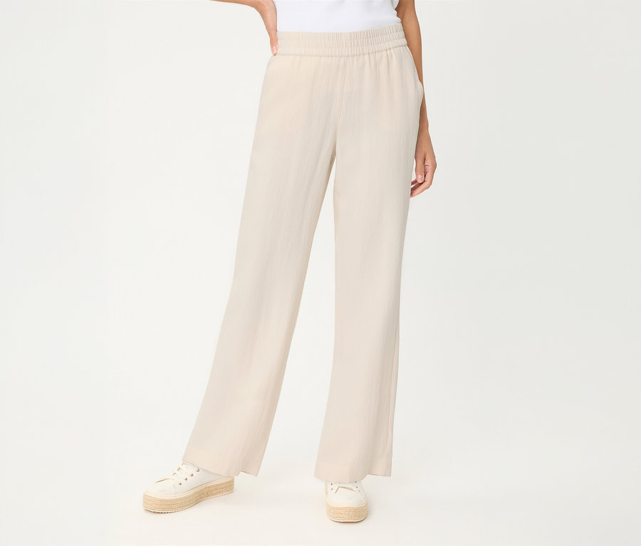 Personne en pantalon en lin Olsen beige clair à jambes larges et taille élastique, avec espadrilles blanches.
