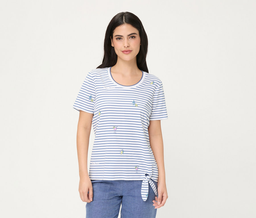 Femme portant un T-shirt Olsen, un haut à manches courtes rayé blanc et bleu avec de petits motifs de verres à cocktail et de tranches de citron, noué sur la hanche gauche, associé à un pantalon bleu.