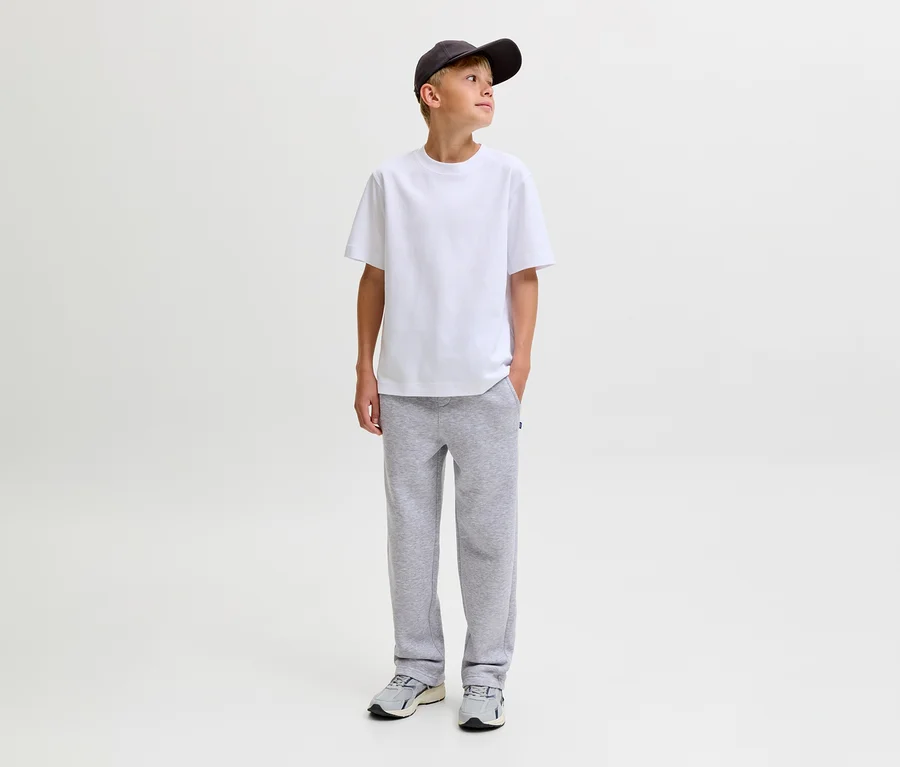 Jeune garçon portant un t-shirt blanc, une casquette de baseball gris foncé et un pantalon de survêtement gris Jack&Jones Bradley, debout les mains dans les poches et regardant à droite.