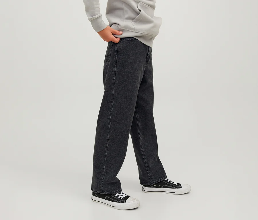 Personne portant un jean noir Jack&Jones JJOriginal Alex, un sweat à capuche gris clair et des baskets noires et blanches, une main tenant la ceinture du jean.
