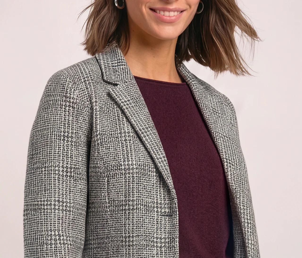 Femme souriante aux cheveux bruns courts portant un blazer Street One à carreaux gris et blanc sur un haut rouge foncé.