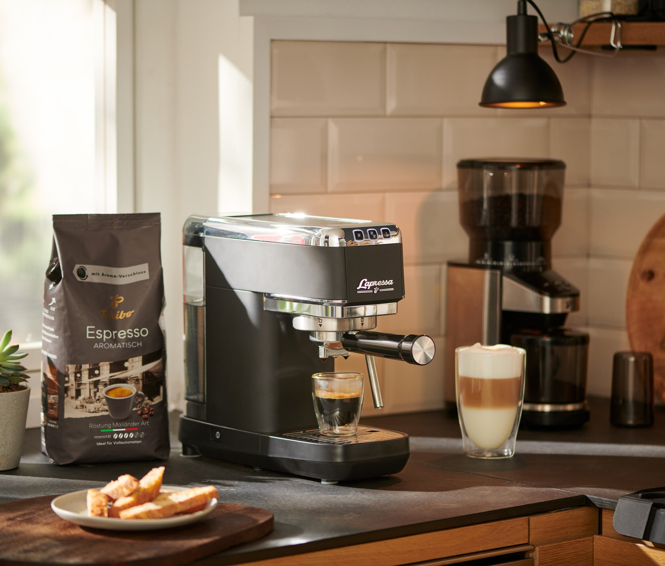 Un expresso coule d'une machine à porte-filtre « Lapressa », noire, dans un verre. Un moulin à café et un paquet de café sont visibles à l'arrière-plan.