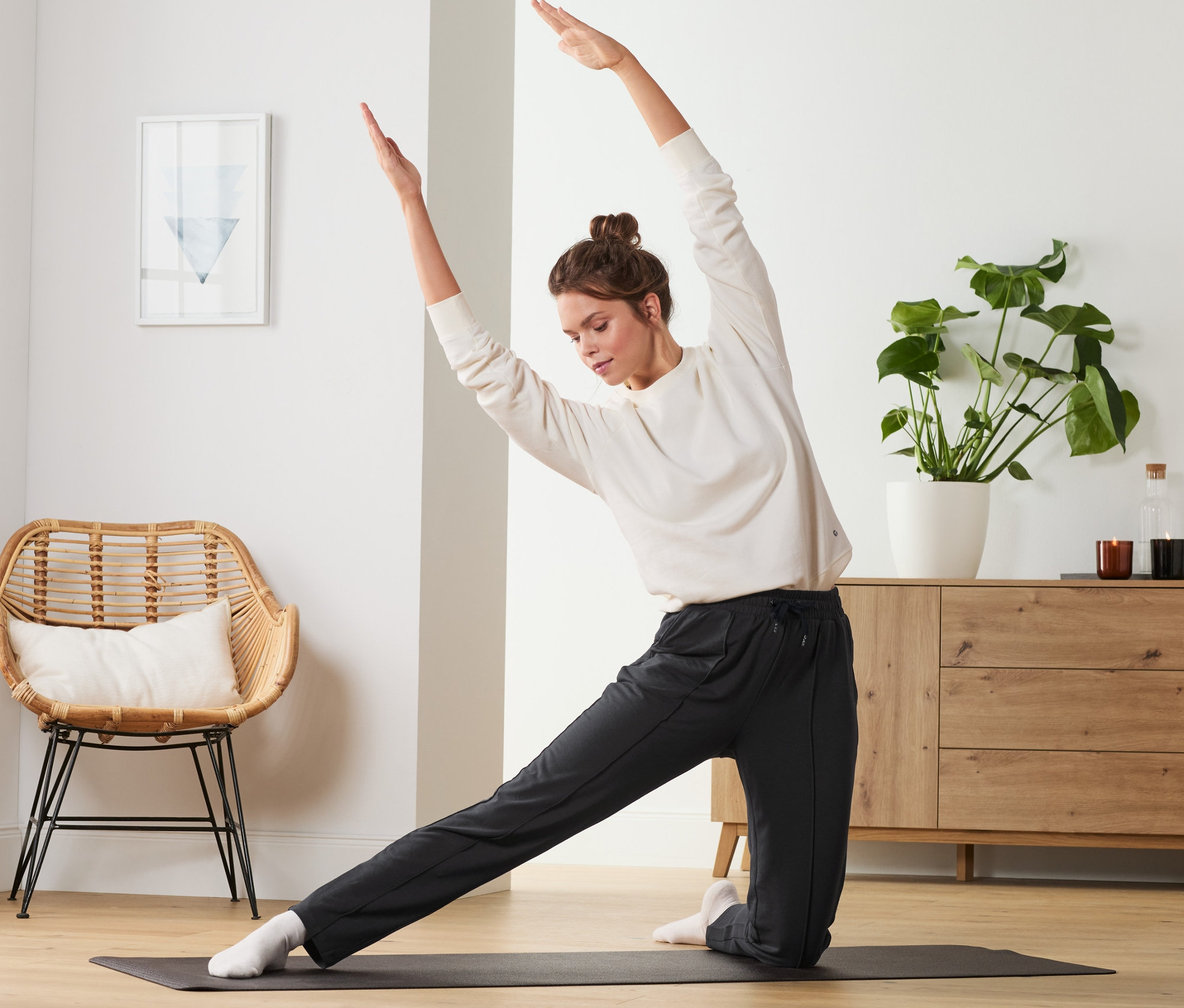 Femme faisant des étirements sur un tapis de yoga, portant un pantalon de jogging noir.