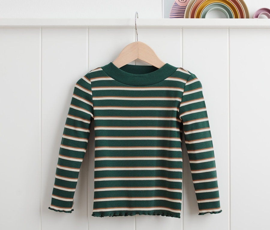 Un t-shirt côtelé à rayures vertes est suspendu à un cintre devant un mur blanc.