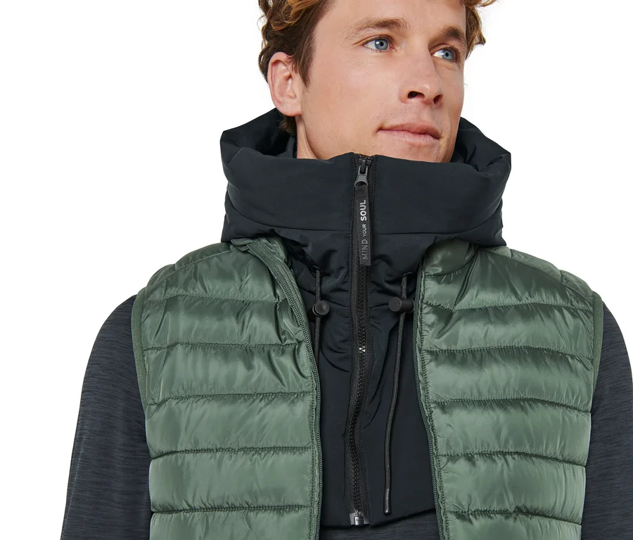 Un homme porte un gilet vert et une capuche matelassée avec col montant.