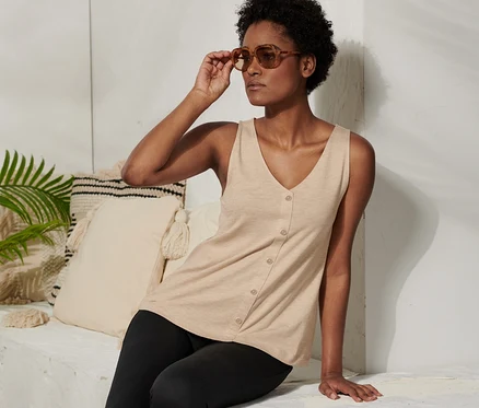 Femme assise ajustant ses lunettes de soleil. Elle porte un haut beige avec patte de boutonnage et un legging noir.