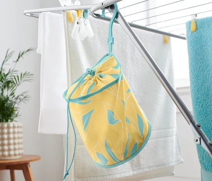Un sac à pinces à linge jaune avec une bordure bleue est suspendu à un séchoir à linge.