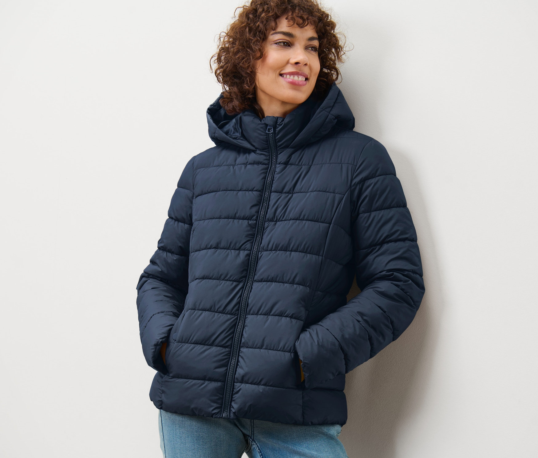 Femme souriant et portant une veste matelassée à capuche bleu foncé.