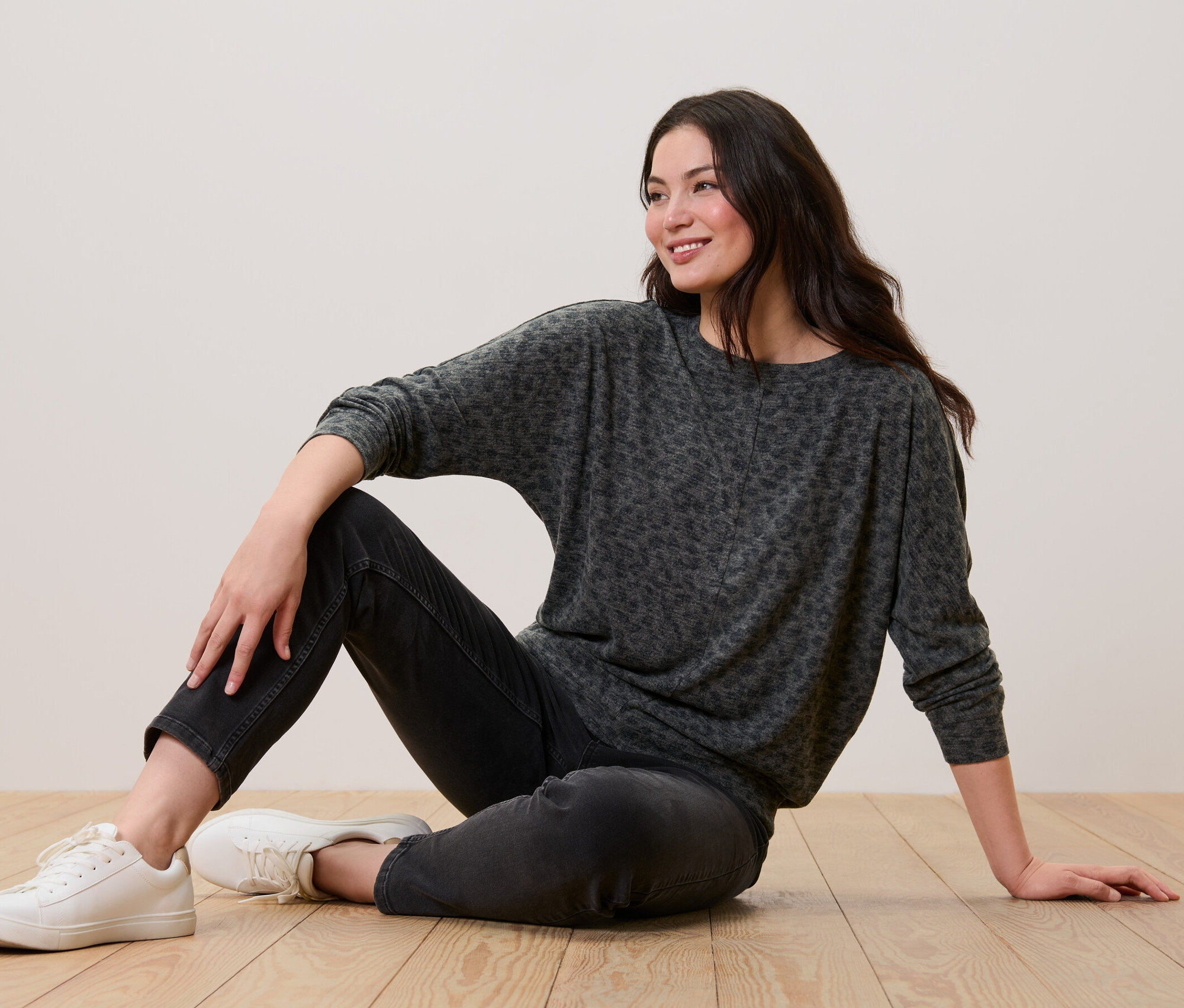 Femme assise par terre portant un t-shirt chauve-souris imprimé, un jean noir et des baskets blanches.