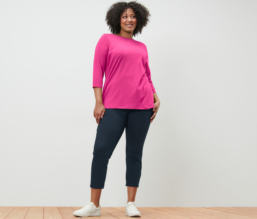 Une femme debout porte un t-shirt rose à manches 3/4 et un jegging 7/8.