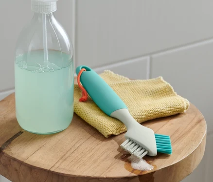 Une brosse à joints, doux/dur est posée sur un chiffon jaune à côté d'un produit de nettoyage.