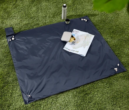 Sur l'herbe verte se trouve une couverture bleu foncé avec une carte, une boîte à lunch en acier inoxydable avec de la nourriture, une gourde et une tasse.