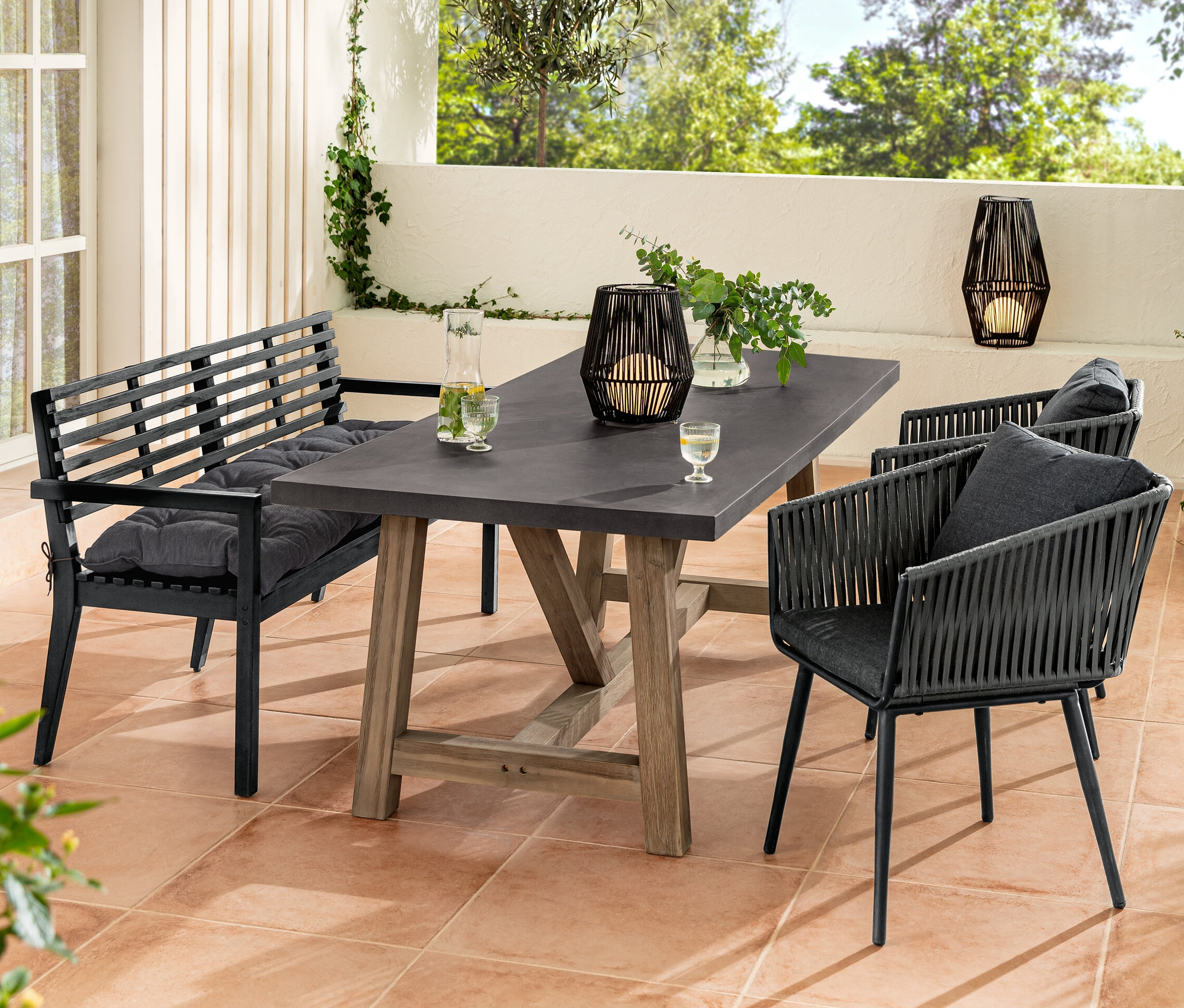 Un ensemble de meubles de jardin avec un banc de jardin et un coussin Sun Garden, une table à manger, des fauteuils avec tressage textile et une lanterne solaire.