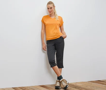Femme appuyée contre un mur portant un t-shirt technique orange.