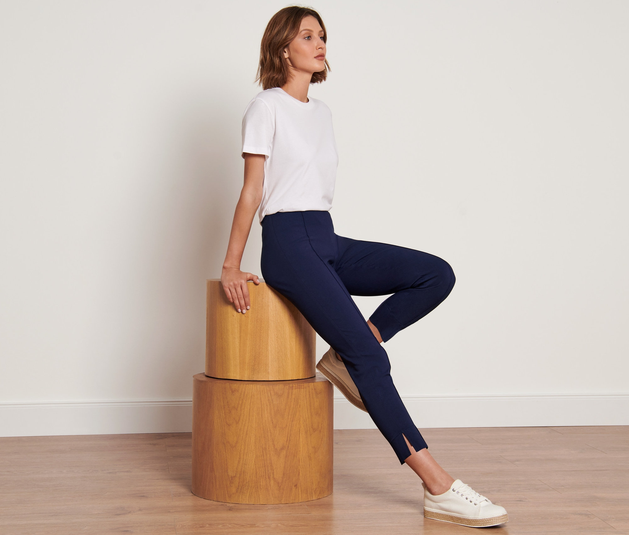 Femme assise sur des cylindres en bois portant un pantalon stretch bleu foncé.