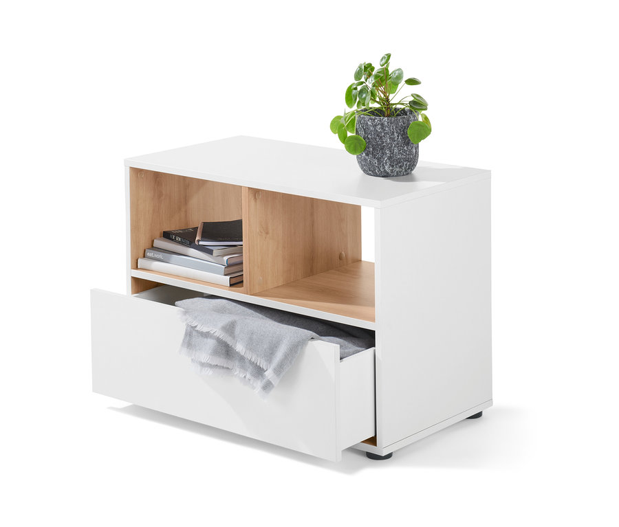 Buffet blanc avec tiroir, sur lequel est posée une plante dans un pot gris. Des livres sont placés dans le compartiment ouvert et une couverture grise dans le tiroir.