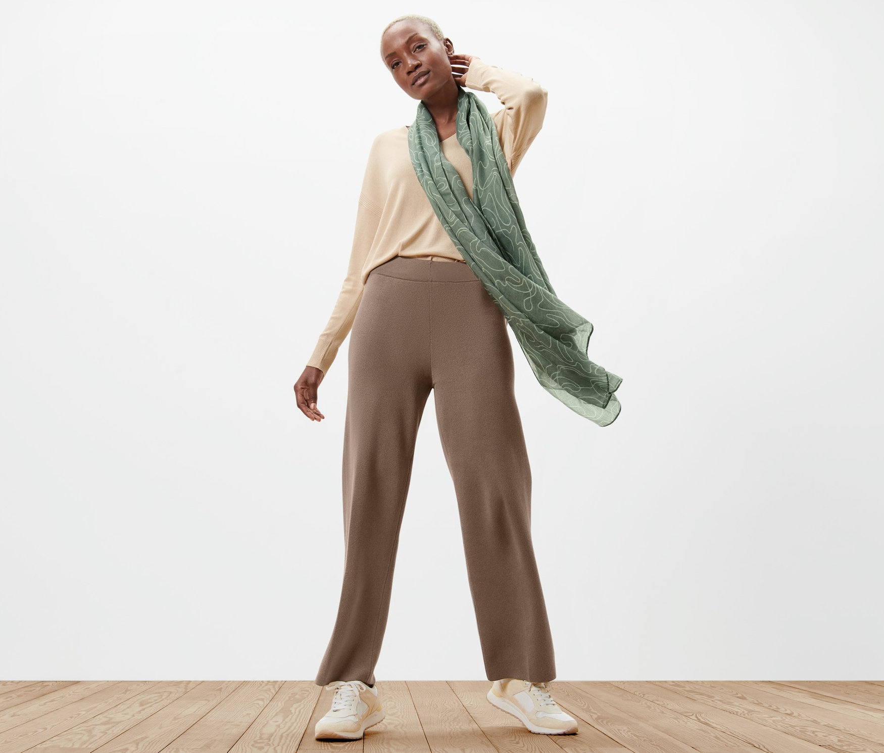 Une femme pose en pantalon en maille, pull et écharpe.