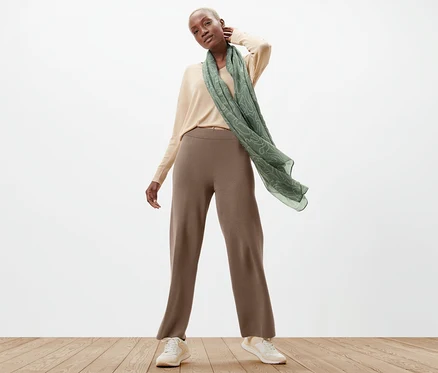 Une femme pose en pantalon en maille, pull et écharpe.