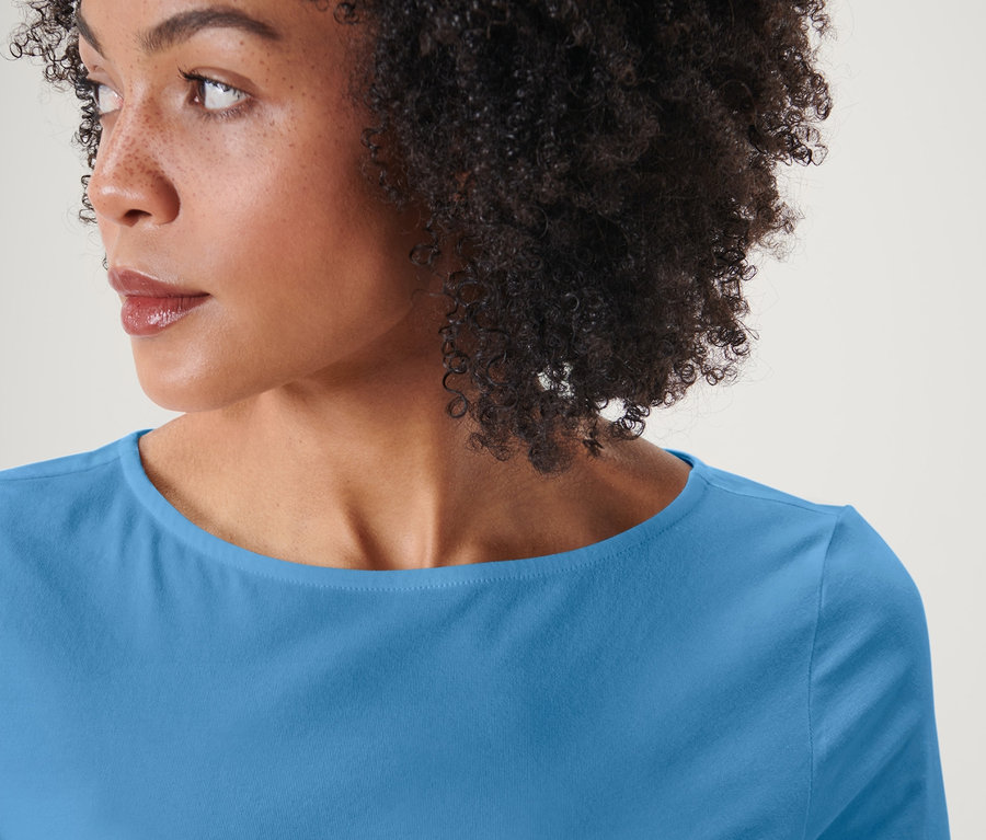 Portrait d'une femme aux cheveux afro portant un t-shirt bleu clair à manches 3/4.