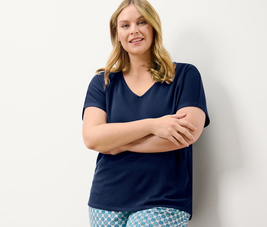 Une femme pose, les bras croisés, portant un chemisier bleu marine texturé et un pantalon en jersey à imprimé intégral.