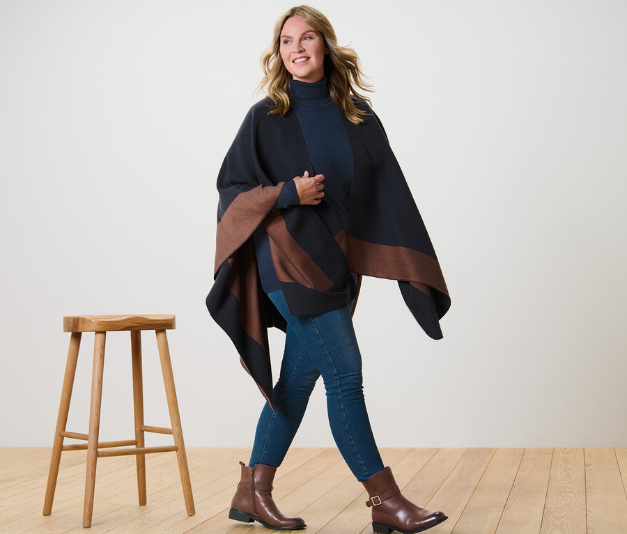 Femme marchant portant un poncho tendance, un pull à col roulé en maille fine bleu foncé et un jegging.