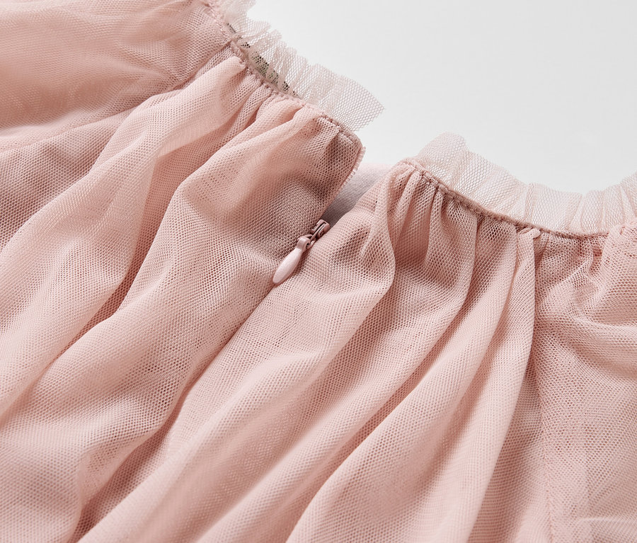 Gros plan sur une robe en tulle rose pour enfant, avec une bordure à volants et une fermeture éclair.