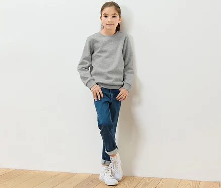 Une fille est appuyée contre un mur blanc et porte un sweat-shirt gris pour enfant avec un intérieur gratté.