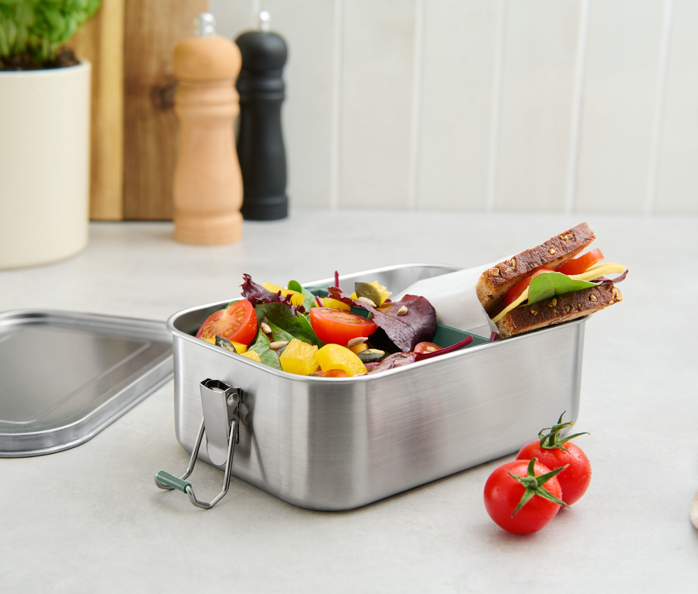 Une boîte à lunch en acier inoxydable remplie de tomates, de salade et d'un sandwich.