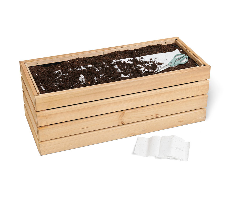 Jardinière en bois avec de la terre, un tapis de graines et des ciseaux. Un tapis de graines « Prairie pour abeilles » est posé dans la jardinière.