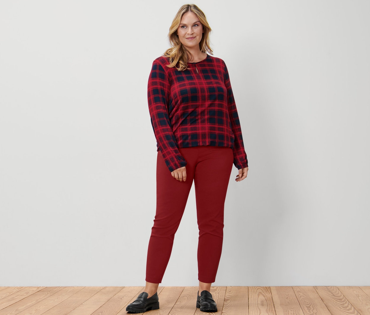 Une femme debout portant une blouse à carreaux, un pantalon stretch rouge et des loafers en cuir.