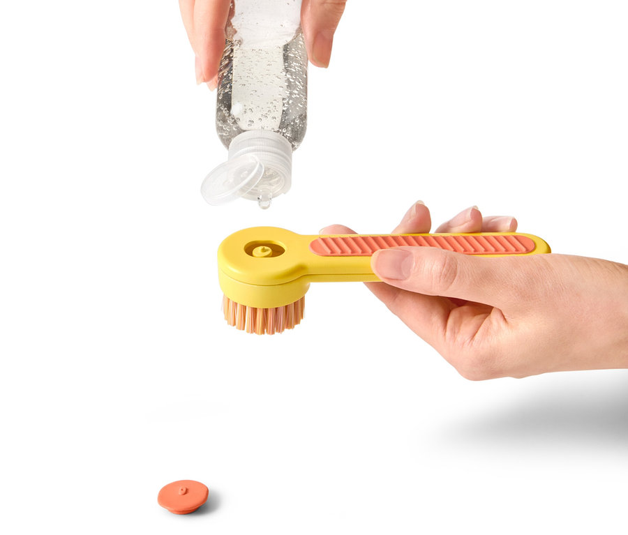 Une main verse une solution de nettoyage sur une brosse à chaussures jaune.