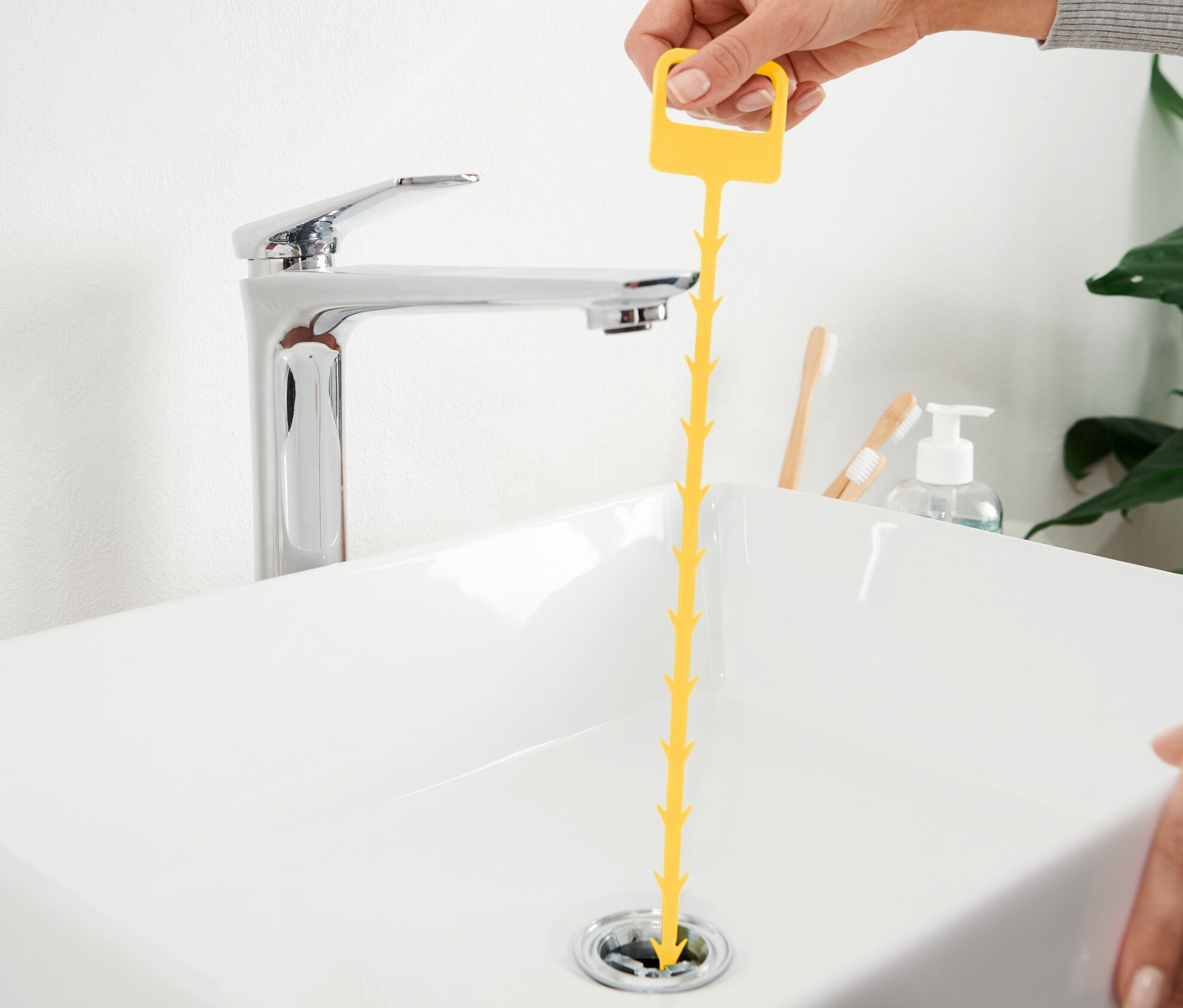 Une main insère une des 2 tiges de curage jaunes dans un lavabo blanc.