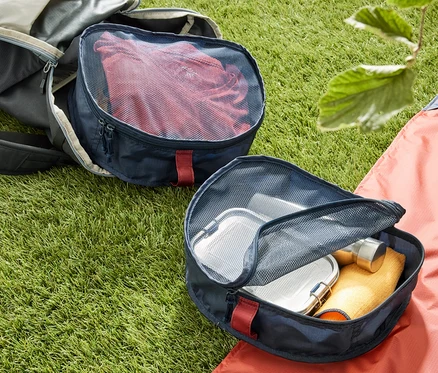 Sur l'herbe reposent un sac à dos ouvert et deux organisateurs de sac à dos. Un organisateur est rempli de vêtements rouges.