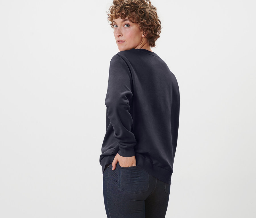 Femme regardant par-dessus son épaule et posant dans un sweat-shirt bleu foncé.