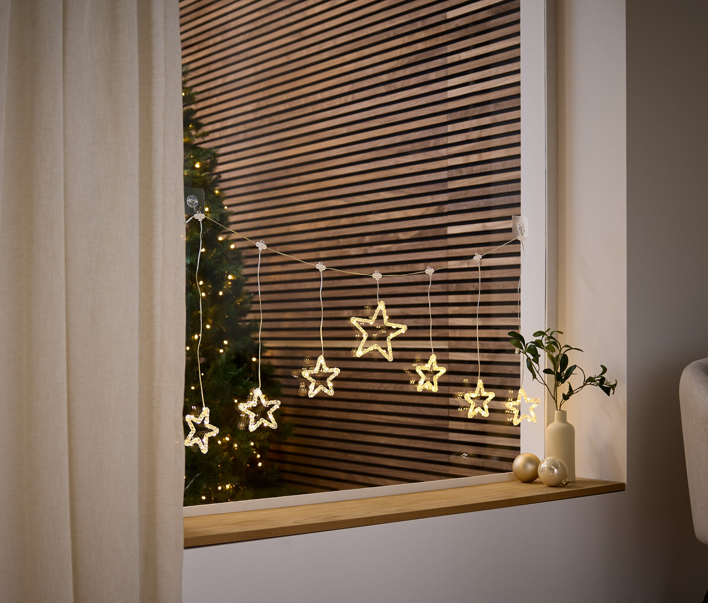 Une guirlande lumineuse en forme d'étoile est suspendue à la fenêtre, derrière laquelle on peut voir un arbre de Noël.