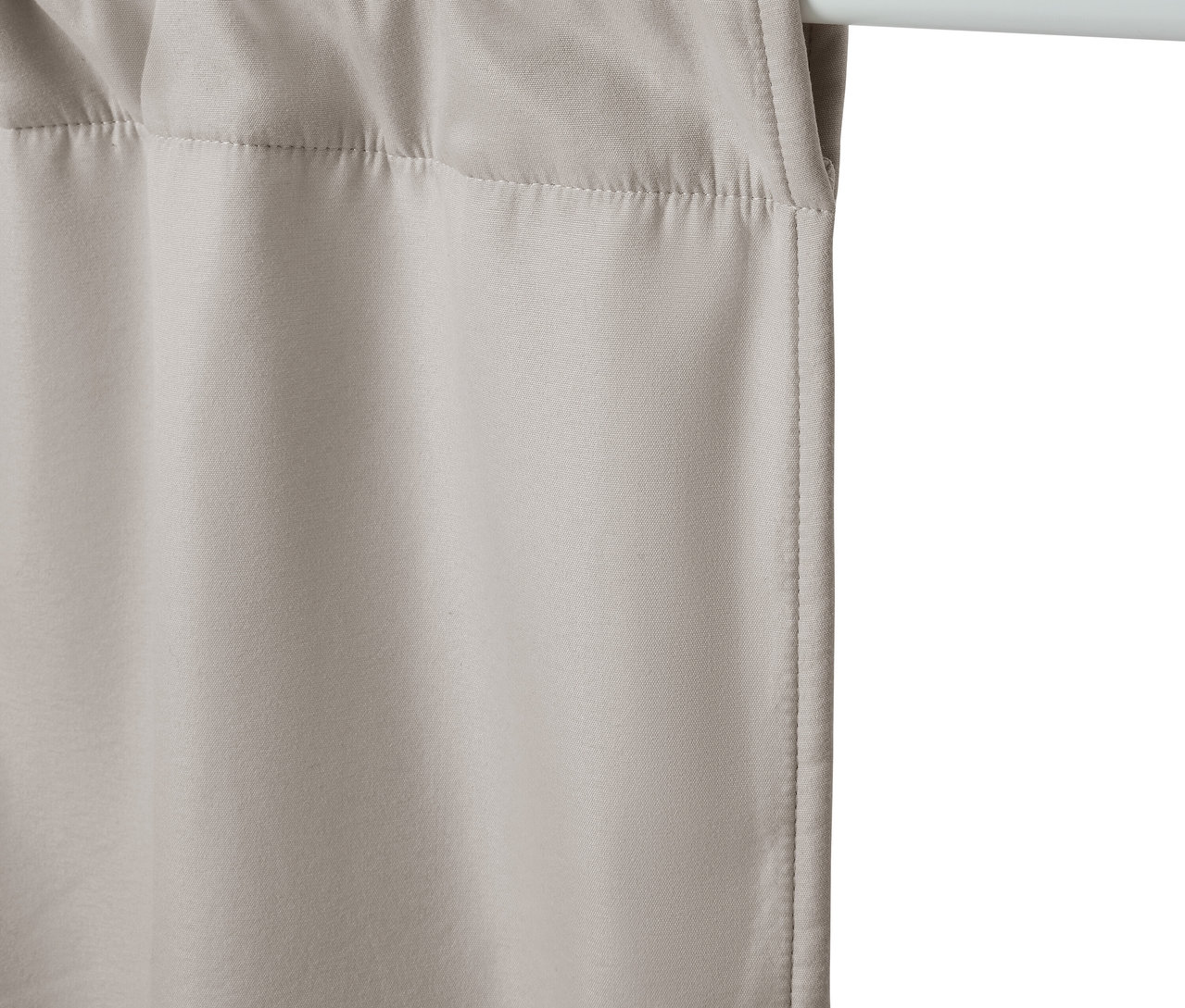 Rideau beige suspendu à une tringle blanche.