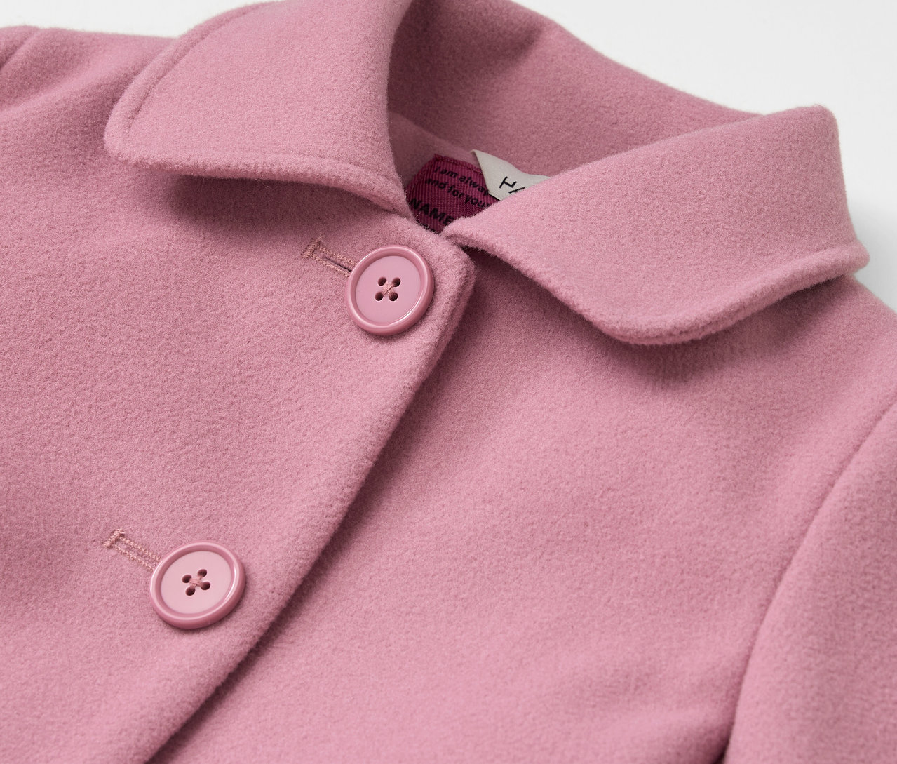 Détail d'un manteau rose avec col et boutons.